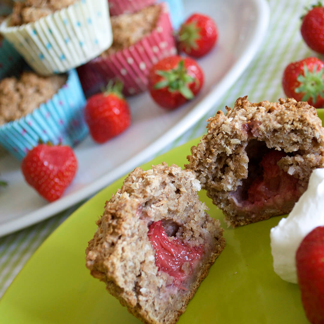 Baby Strawberry Muffins on a serving dish with some strawberries, next to a plate with a muffin cut in half