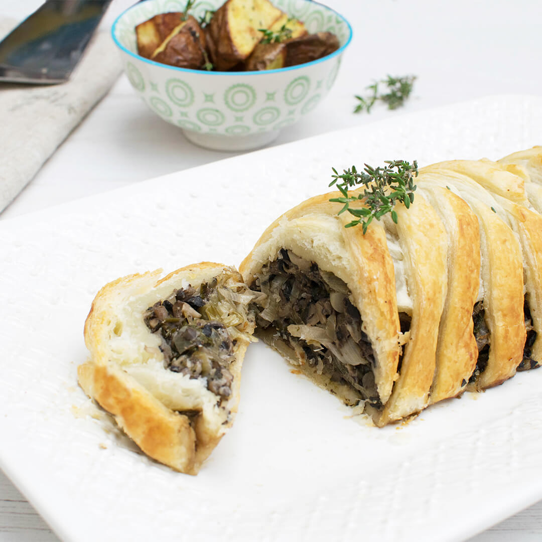 Sliced mushroom and leek wellington next to a bowl of roast potatoes