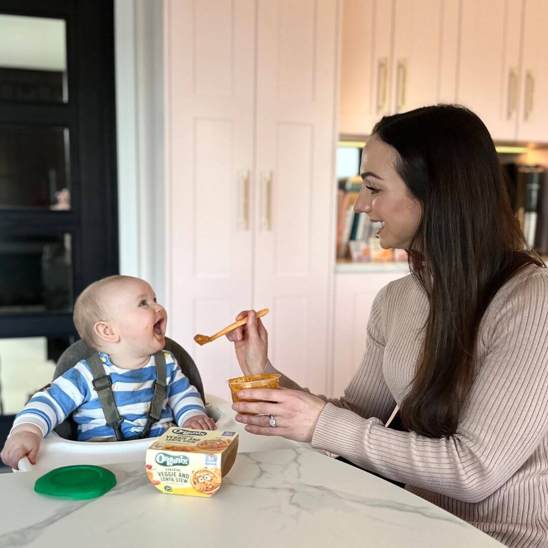 Organix nutritionist expert Mummynutrition and her baby she's feeding the baby Organix meals in a pot. Both smiling. 