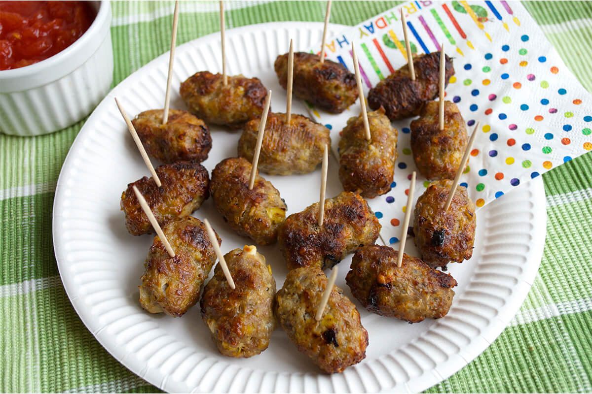 Pork, Leek & Feta Cocktail Sausages on a plate next to a tomato dip