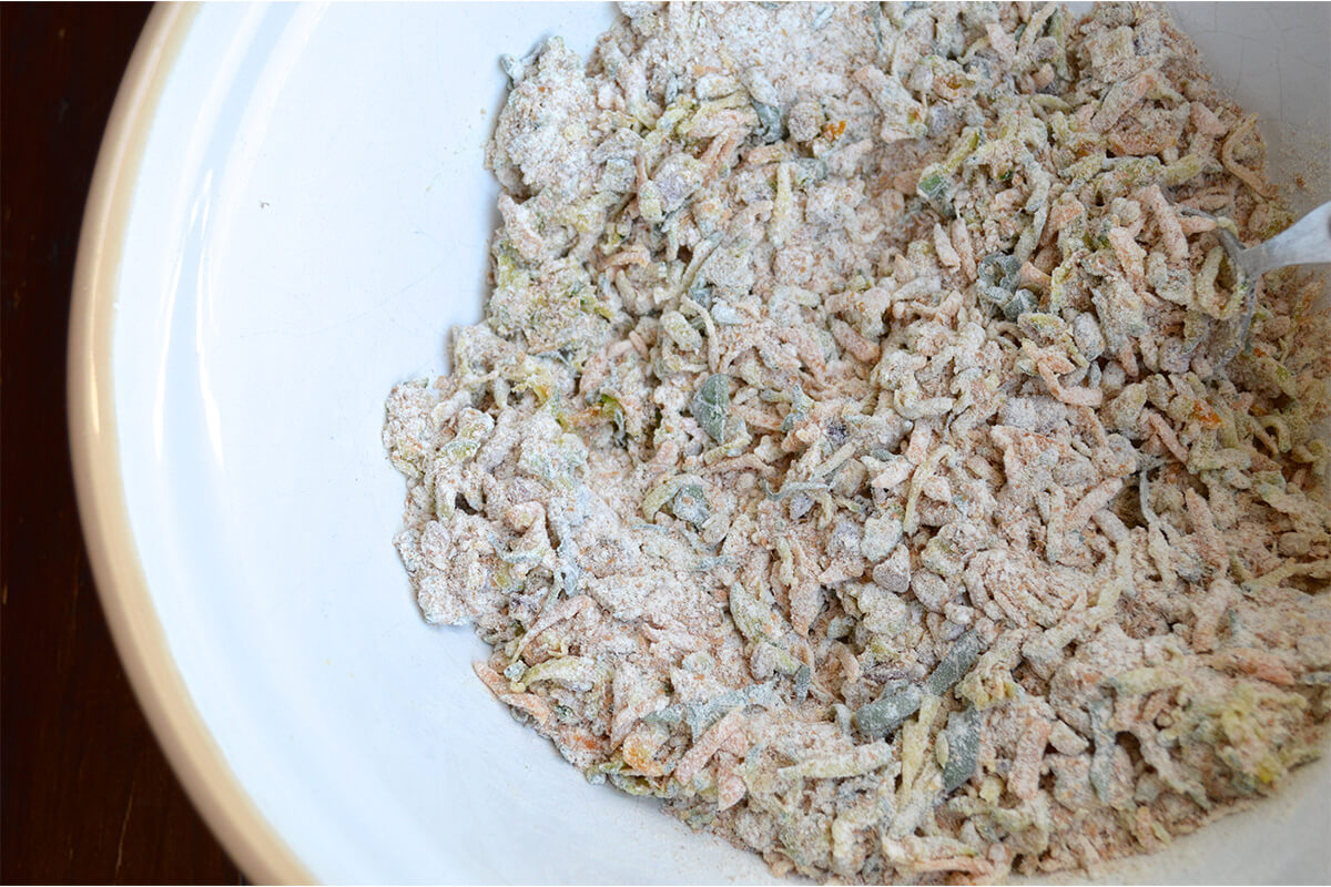 A mixing bowl of flour, vegetables, basil and oil