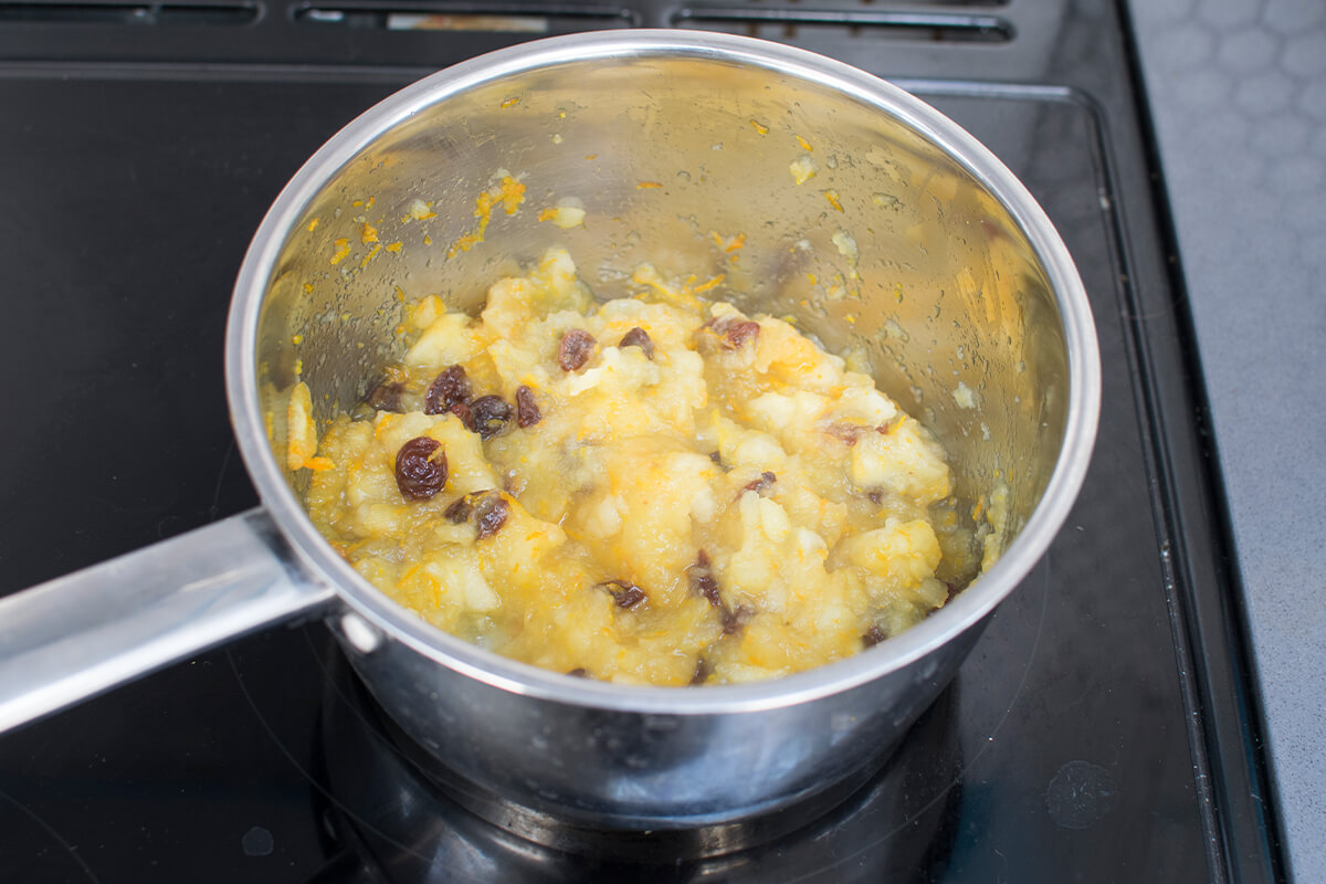 A saucepan with apple, honey, orange zest and raisins