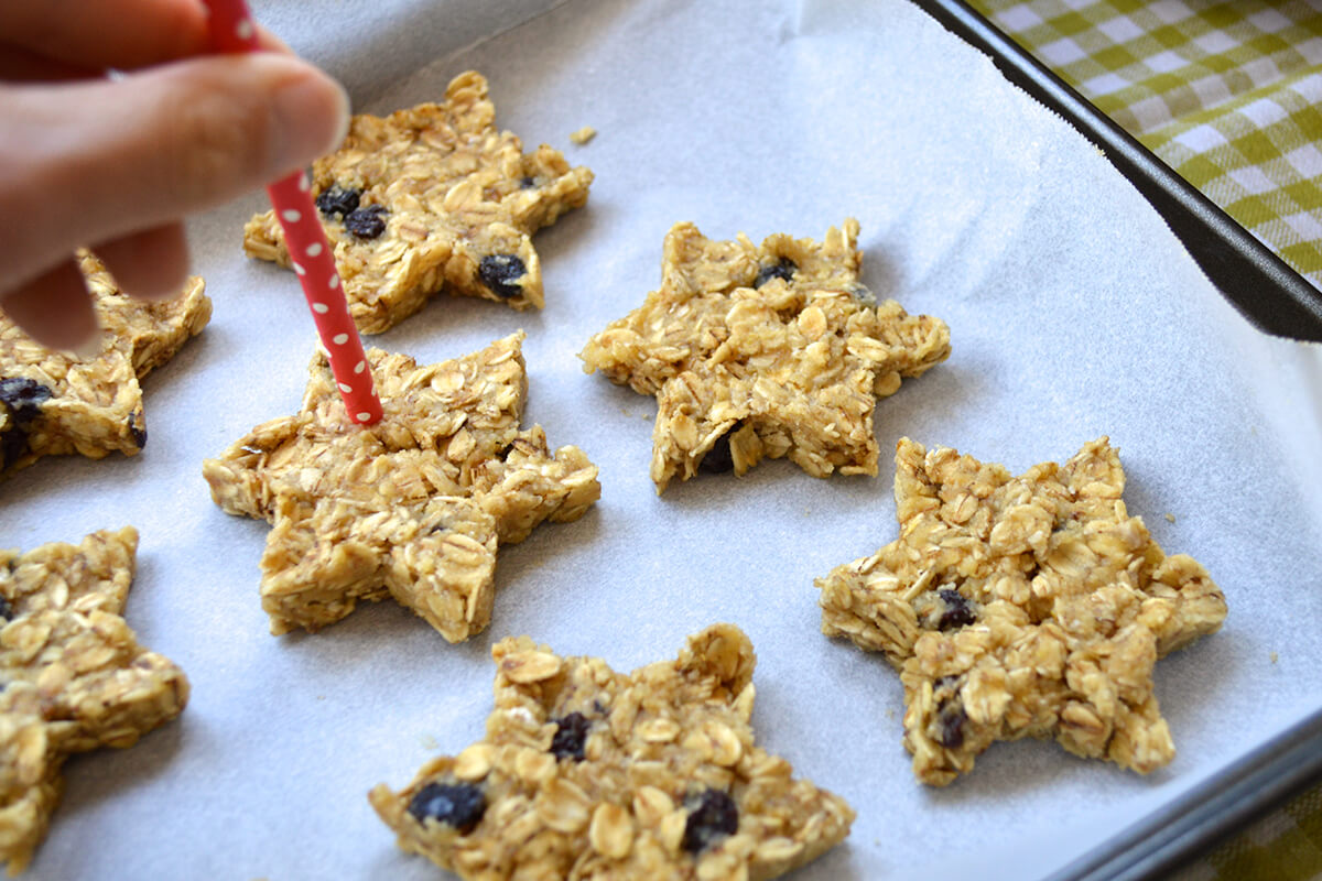 Star shaped biscuits on a line baking, being pierced with a straw to create holes