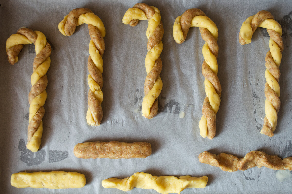 A baking tray lined with parchment paper with uncooked Cheese Straw Christmas Canes on it