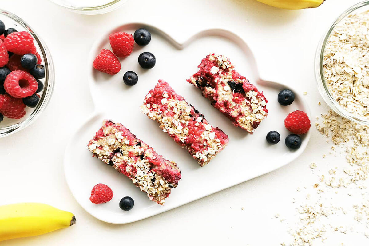 A plate of porridge fingers served with raspberries and blueberries, next to some bananas