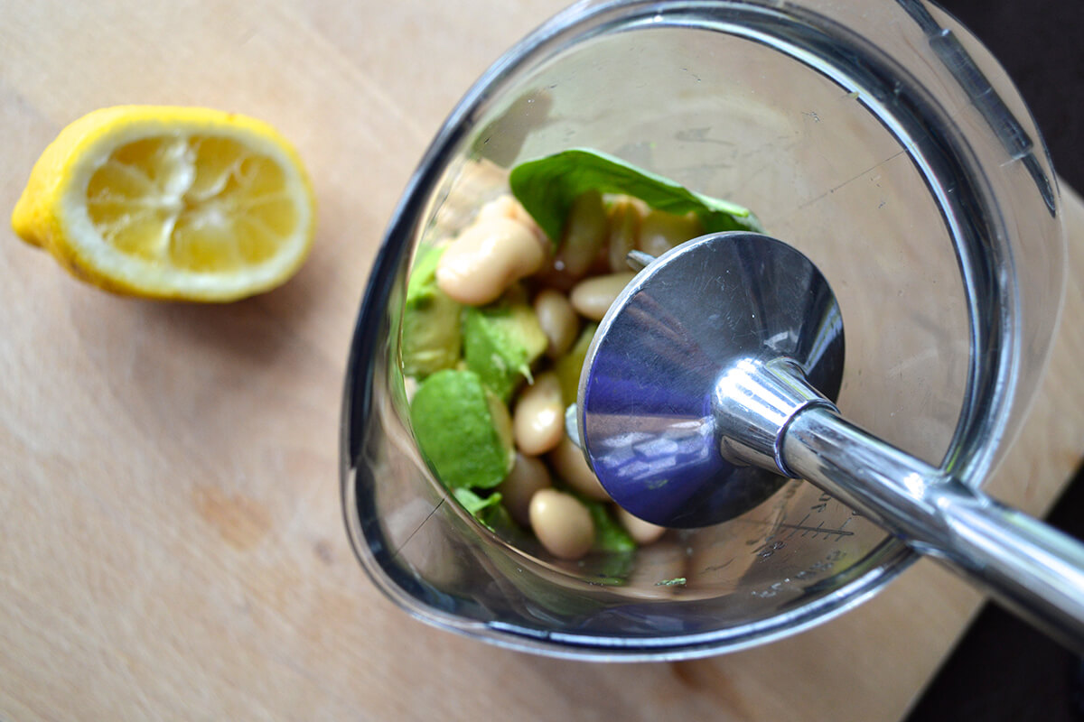 A bowl of butterbeans, half an avocado and basil leaves being mashed