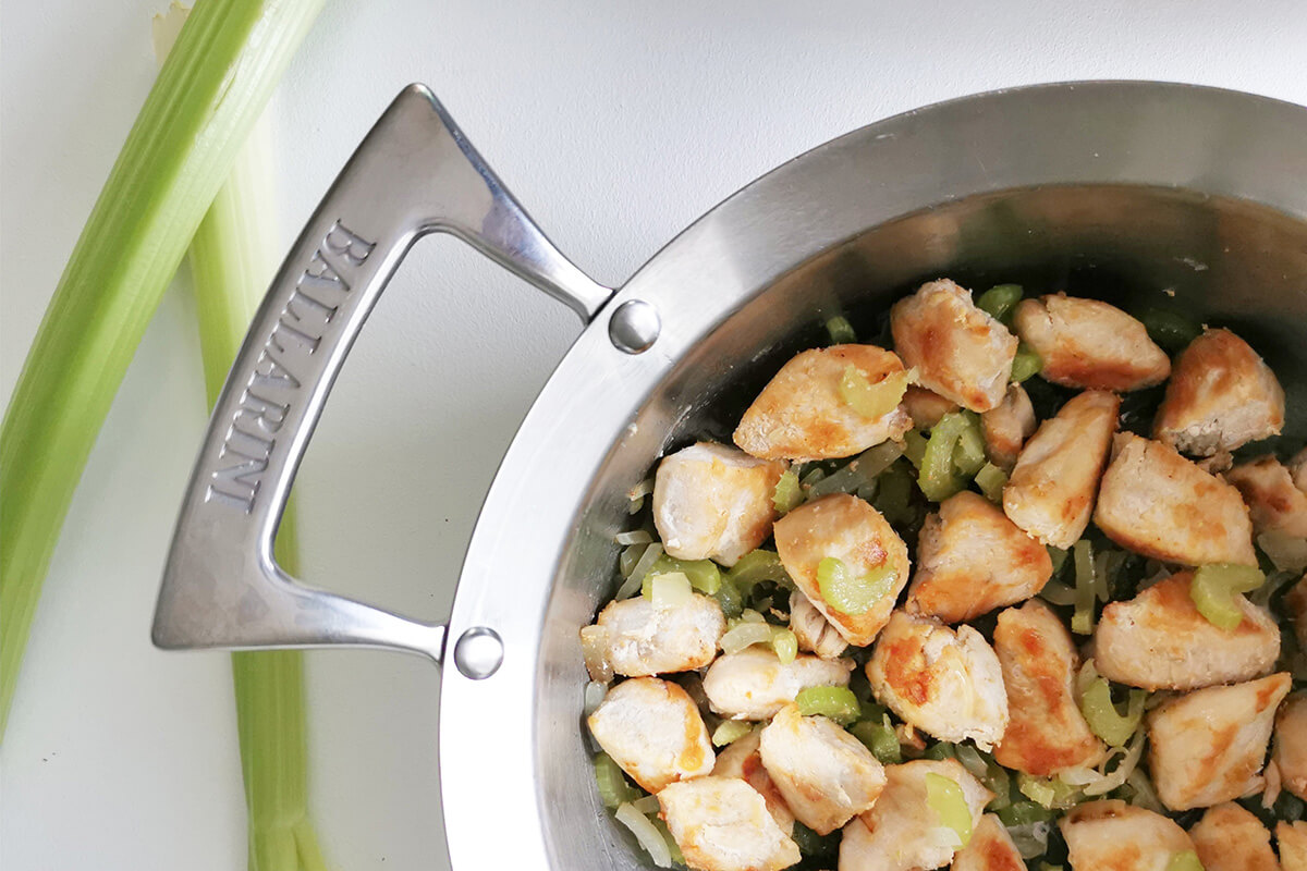 A saucepan with onion, celery and diced chicken being sauteed