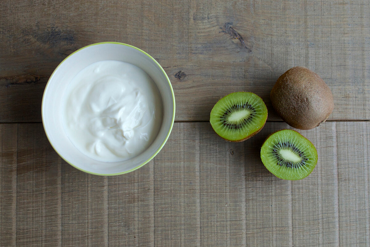 A bowl of yoghurt next to a halved kiwi and a whole kiwi