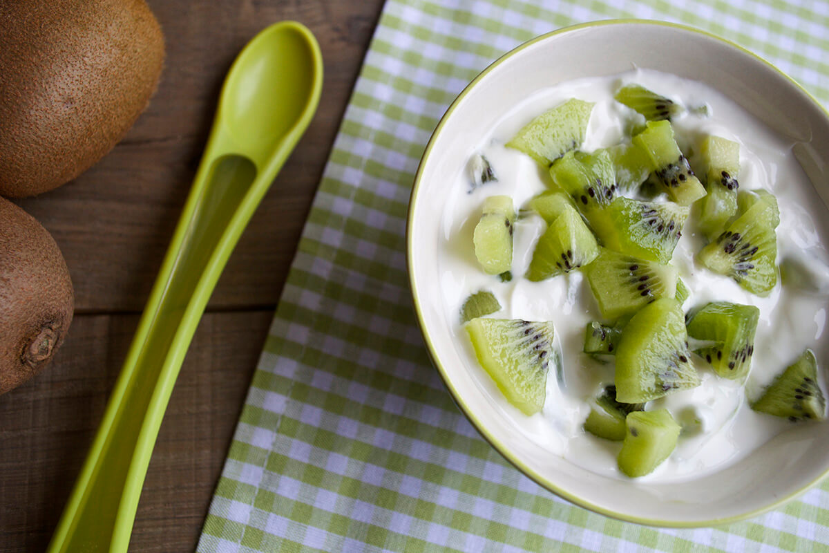 A bowl of yoghurt and kiwi next to two whole kiwis