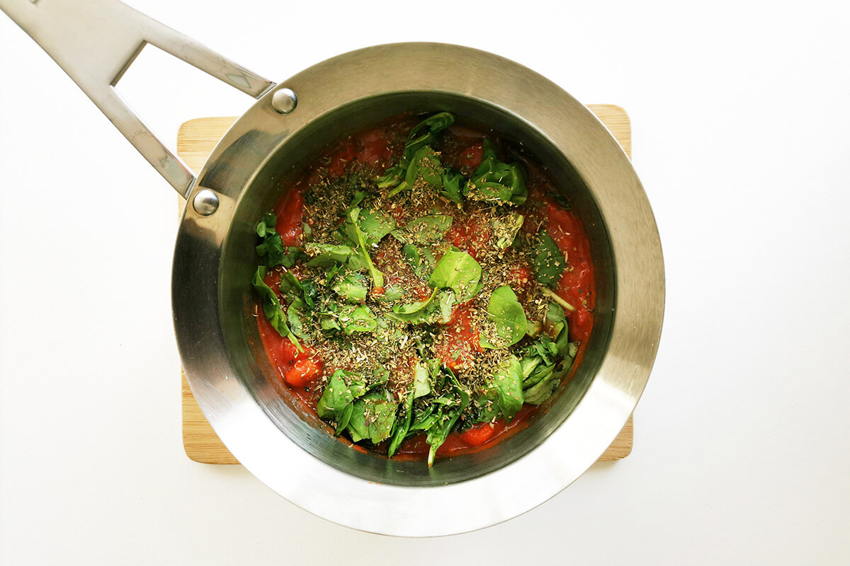 A pan with chopped tomatoes, herbs and fresh spinach