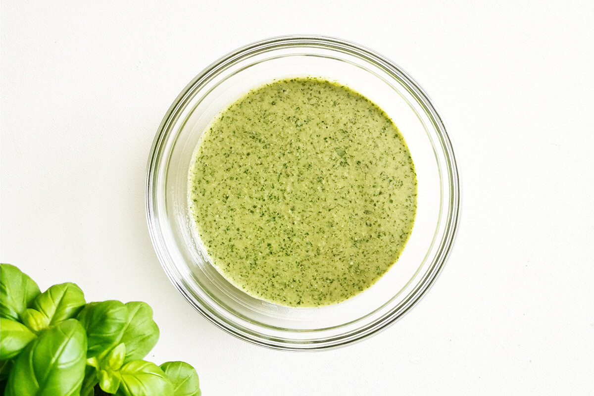 Pesto pasta sauce in a glass bowl next to some basil leaves