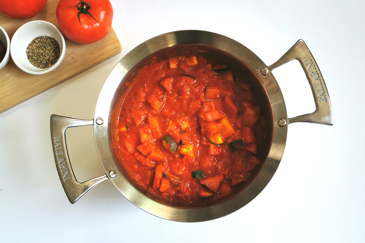 A saucepan of sauteed onions and garlic with cubed aubergine and courgette and chopped tomatoes