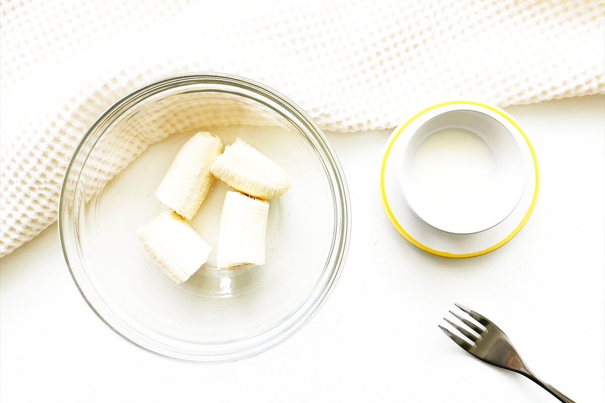 Peeled banana in a glass bowl. There's a small bowl of milk next to it