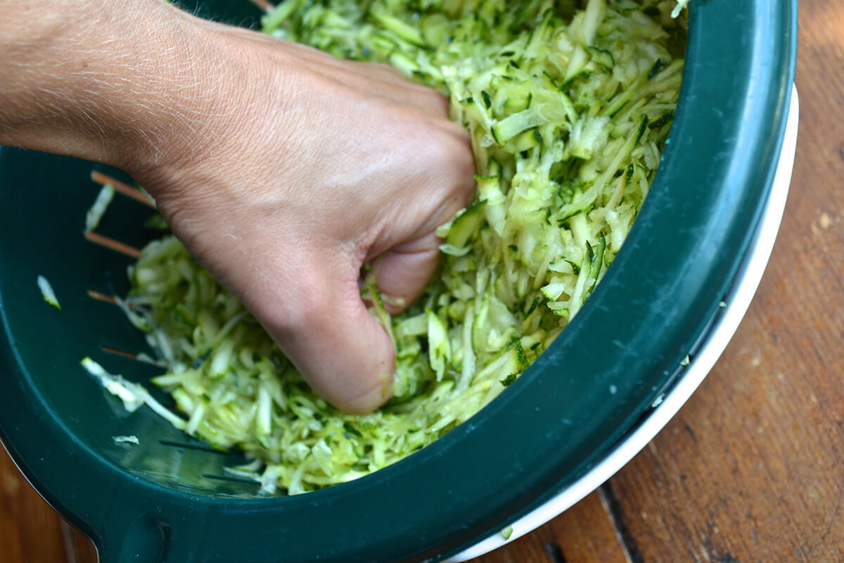 Grated courgette in a sieve, with excess water being squeezed out of it