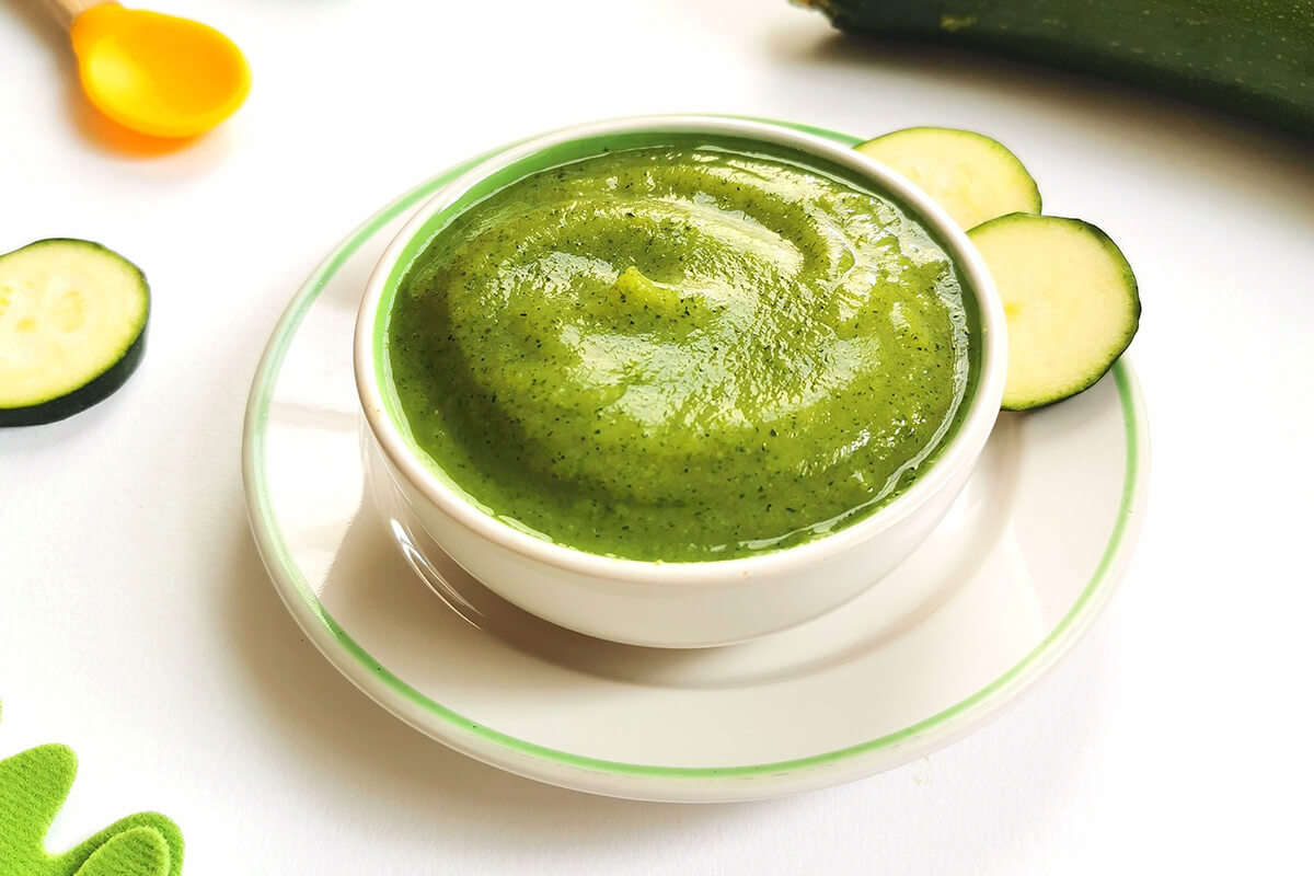 Courgette puree in a small bowl next to a whole courgette and some courgette slices