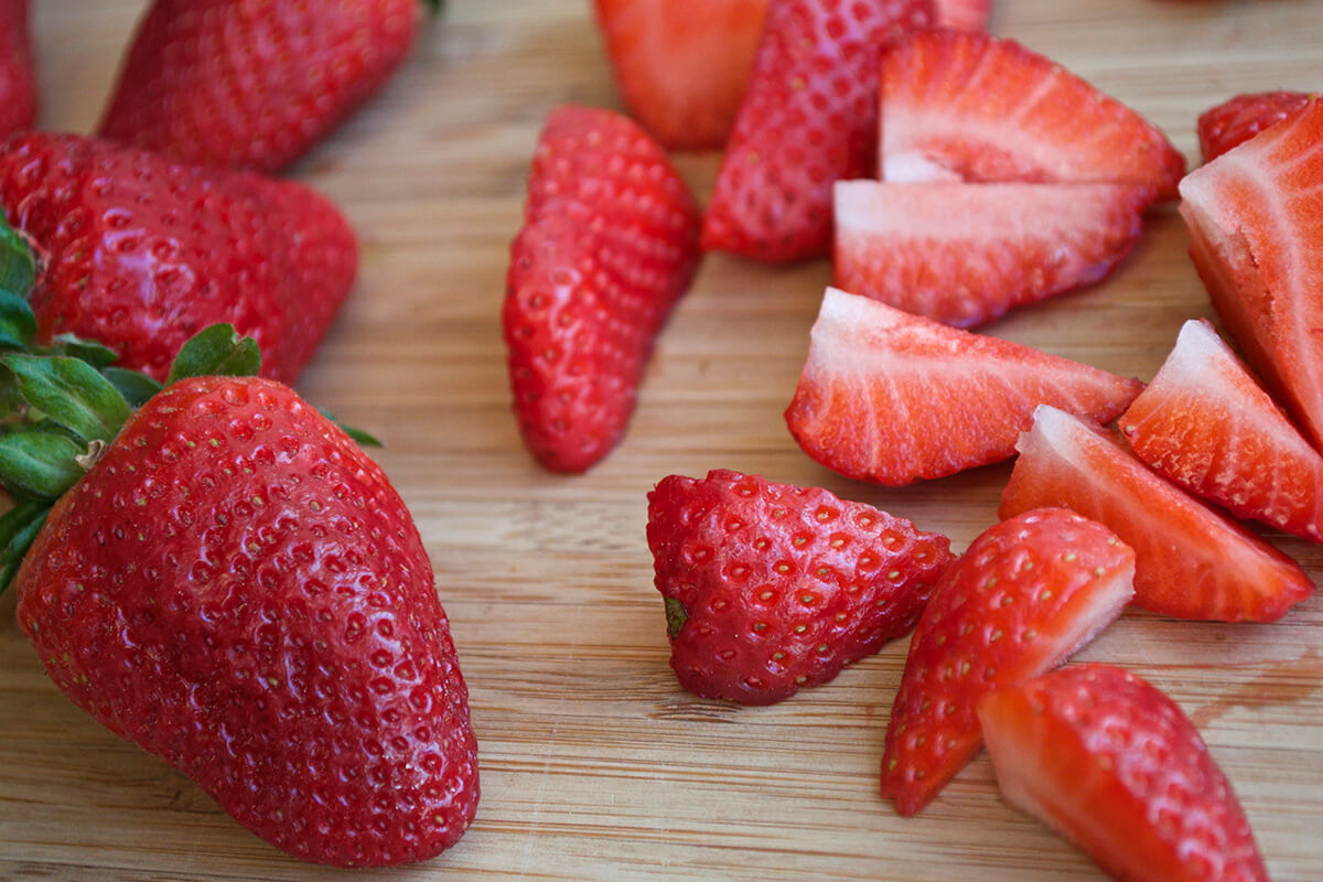 Quartered strawberries on a chopping board next to some whole strawberries