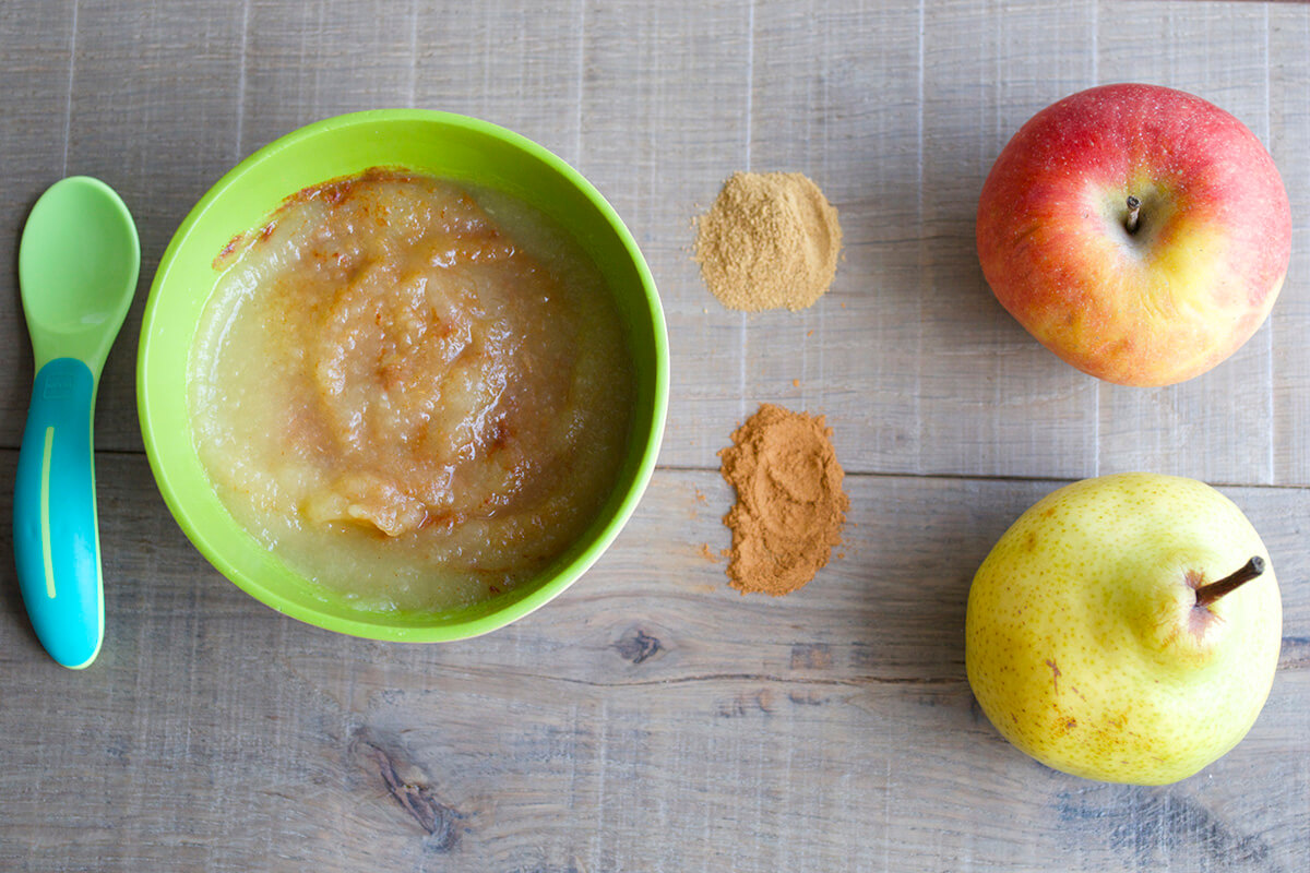 A bowl of Spiced Apple & Pear puree next to a whole apple and pear and some cinnamon